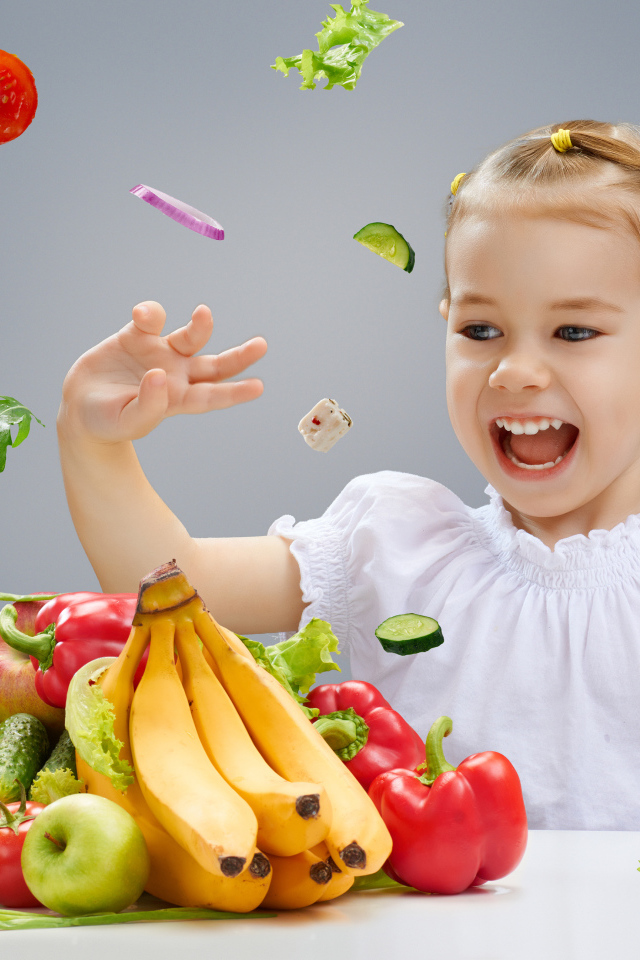 Маленькая девочка играет с овощами и фруктами на кухне