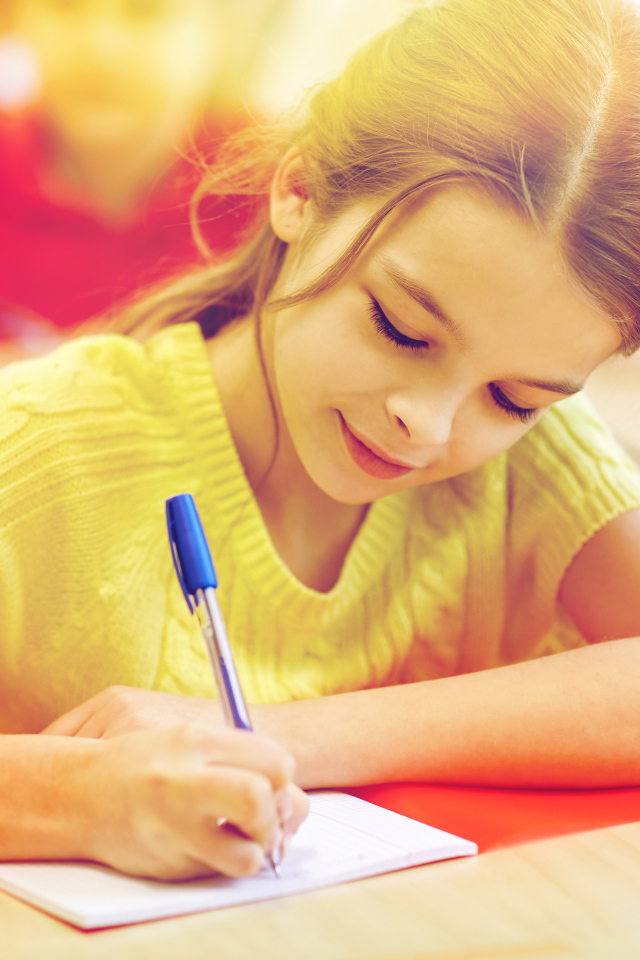 Маленькая девочка школьница пишет ручкой в тетради