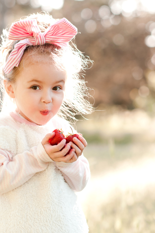 Маленькая девочка с бантом на голове ест клубнику
