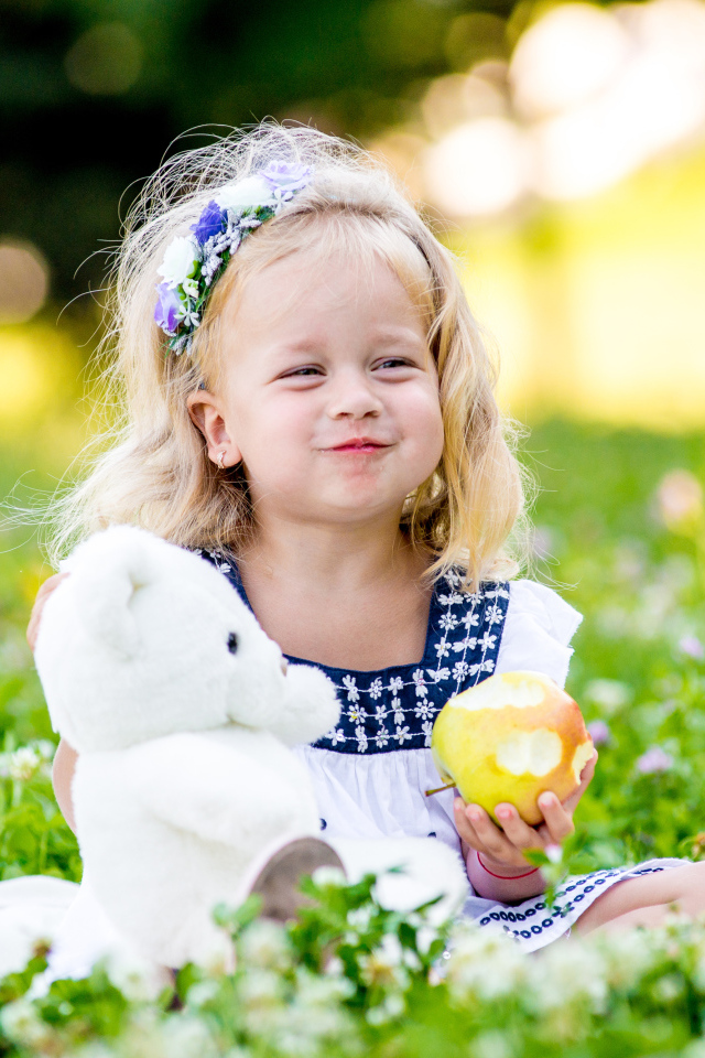 Маленькая девочка с белым медвежонком в руках и большим яблоком