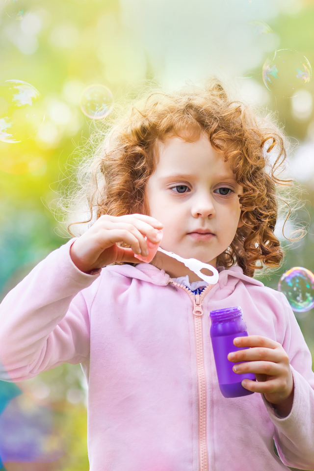 Маленькая рыжеволосая кудрявая девочка с мыльными пузырями