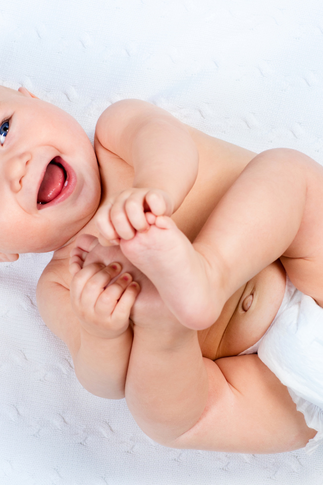 Маленький улыбающийся грудной ребенок держит руками ноги