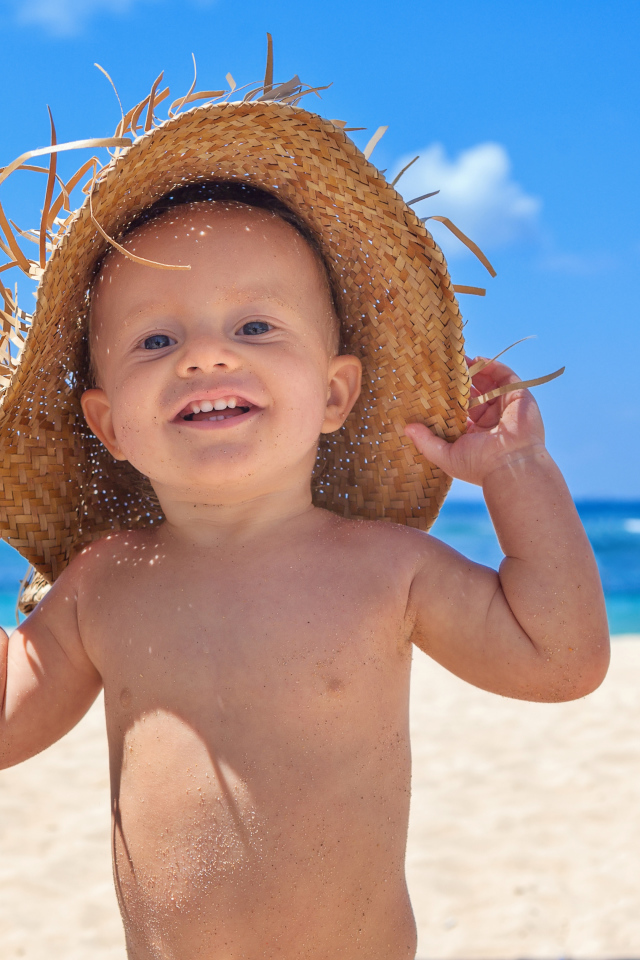 Маленький улыбающийся мальчик в соломенной шляпе на пляже