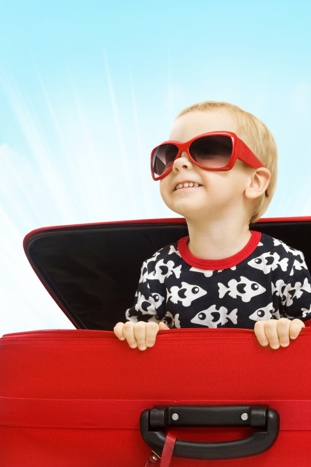 Маленький улыбающийся мальчик в очках сидит в красном чемодане