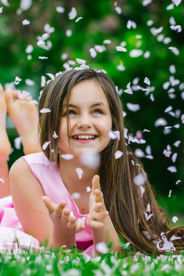 Маленькая улыбающаяся девочка шатенка ловит лепестки