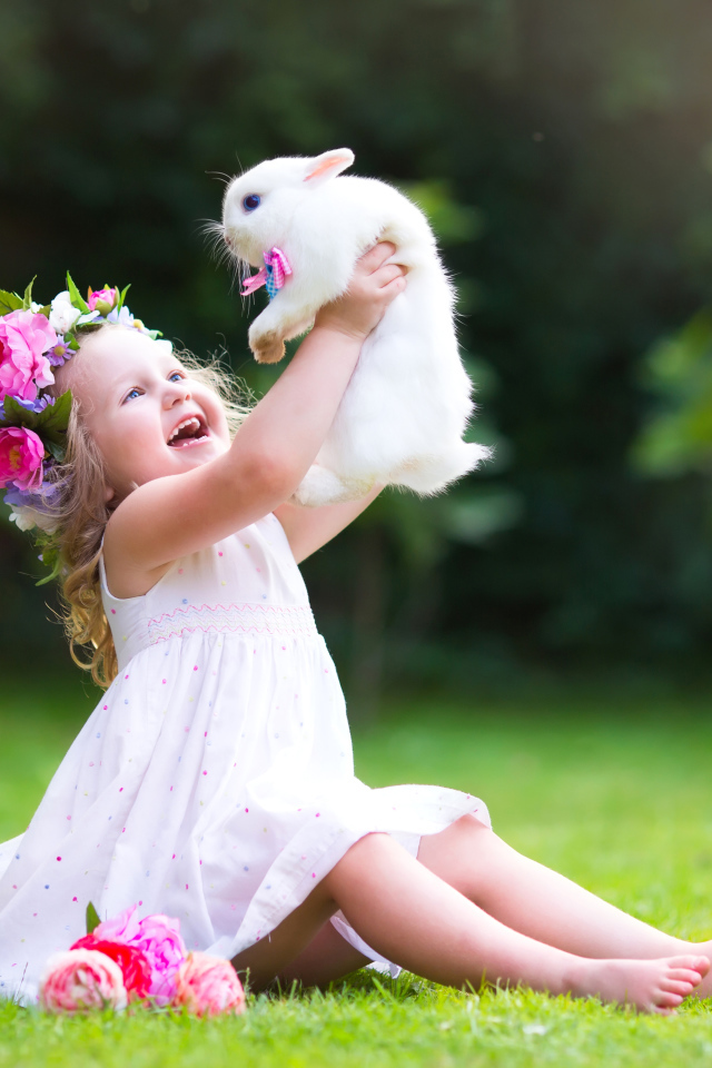Маленькая улыбающаяся девочка держит в руках белого кролика