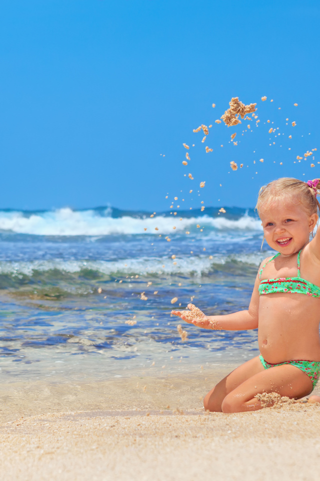 Маленькая улыбающаяся девочка играет на пляже с песком