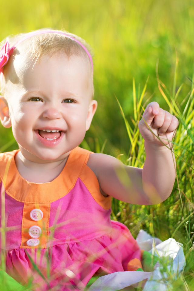 Маленькая улыбающаяся девочка сидит в зеленой траве