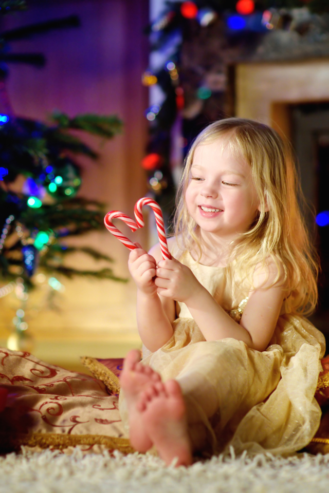 Длинноволосая девочка блондинка с леденцами у новогодней елки