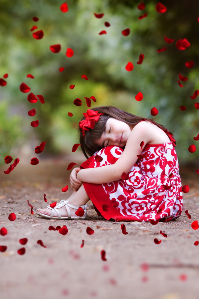 Лепестки красной розы падают на маленькую девочку