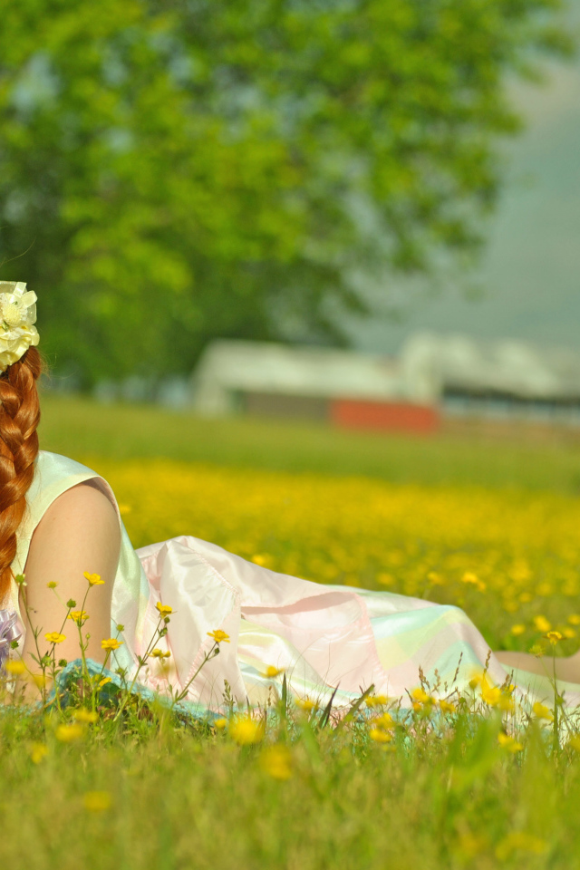 Рыжеволосая девочка с косичками лежит на зеленой траве