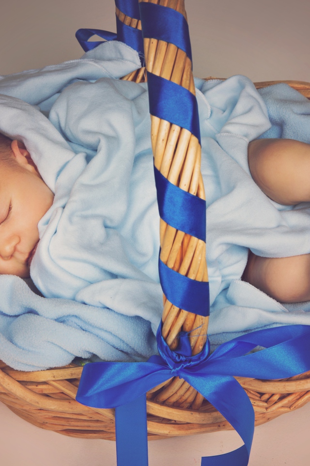 Спящий грудной ребенок в корзине с синими лентами