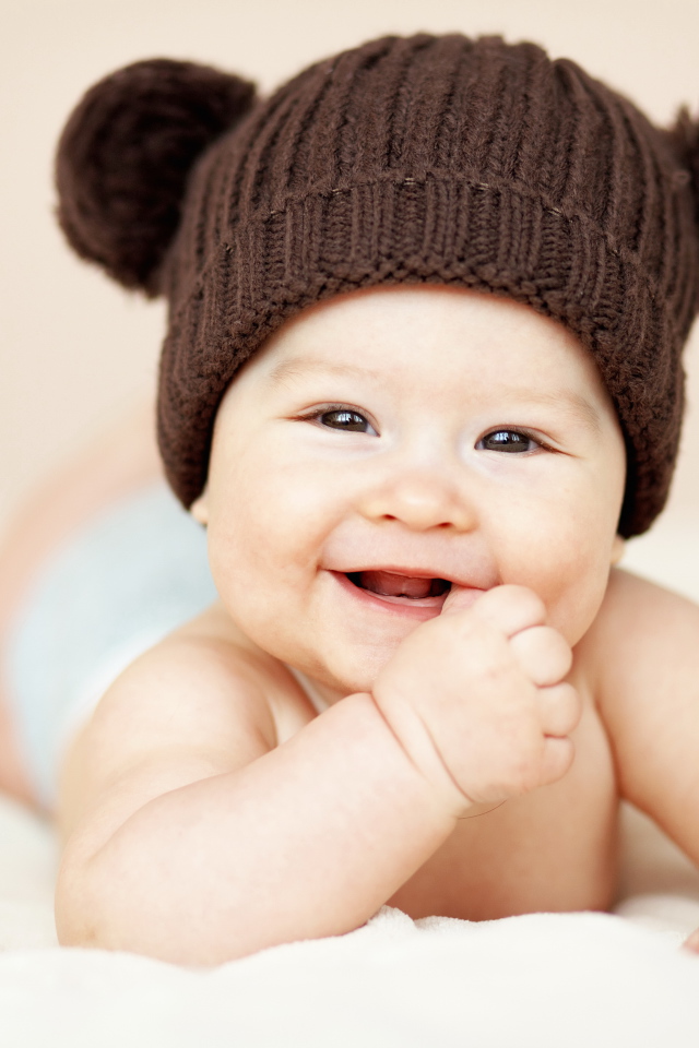 Улыбающийся грудной ребенок в коричневой вязаной шапке