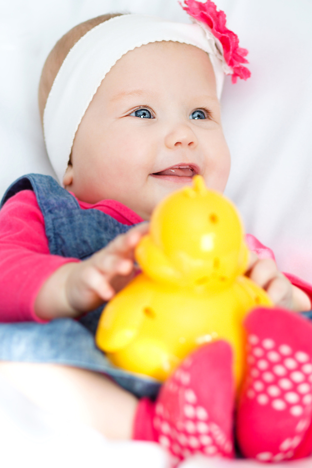 Улыбающаяся голубоглазая девочка младенец с игрушкой в руках