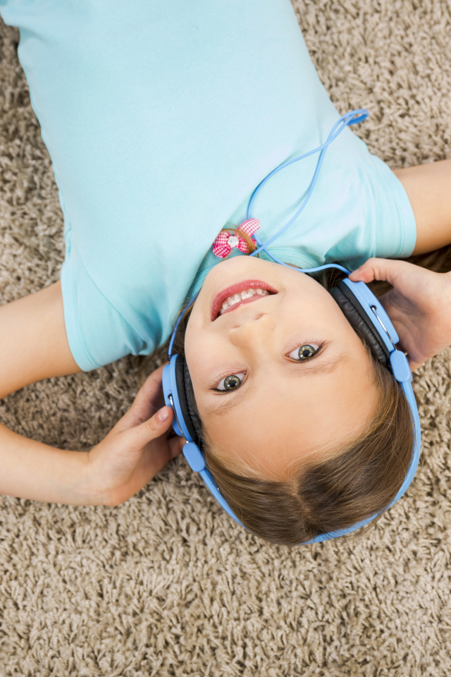 Улыбающаяся девочка в больших голубых наушниках