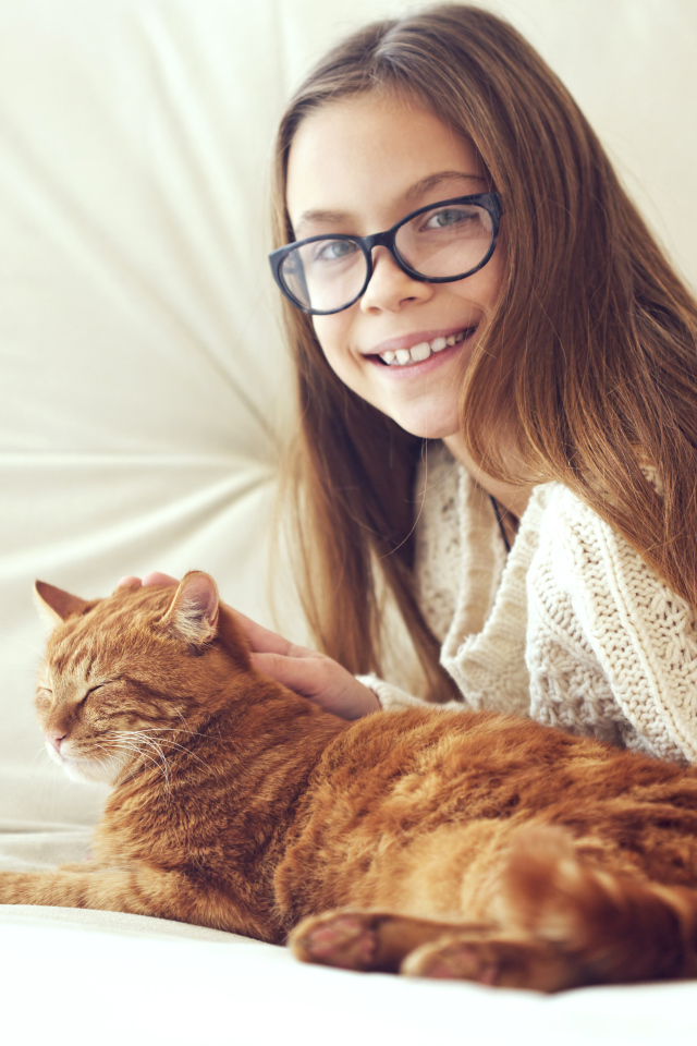 Улыбающаяся девочка шатенка в очках гладит рыжего кота