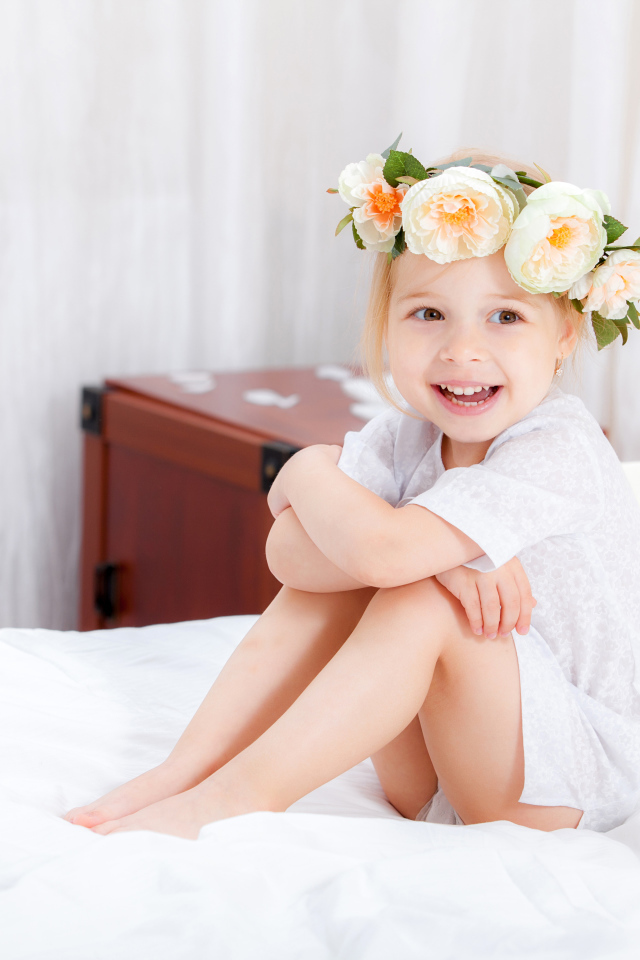 Улыбающаяся девочка с венком на голове сидит на кровати