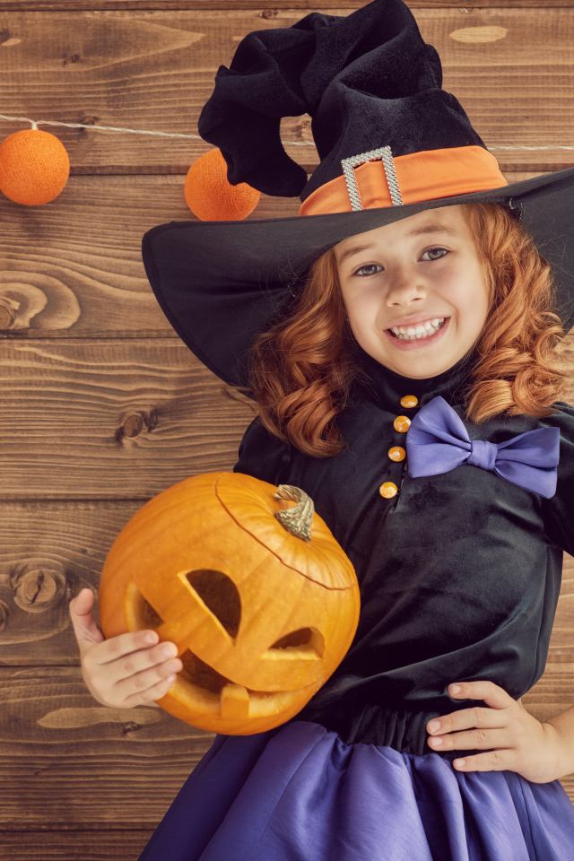 Улыбающаяся маленькая девочка в костюме ведьмы с тыквой на Хэллоуин
