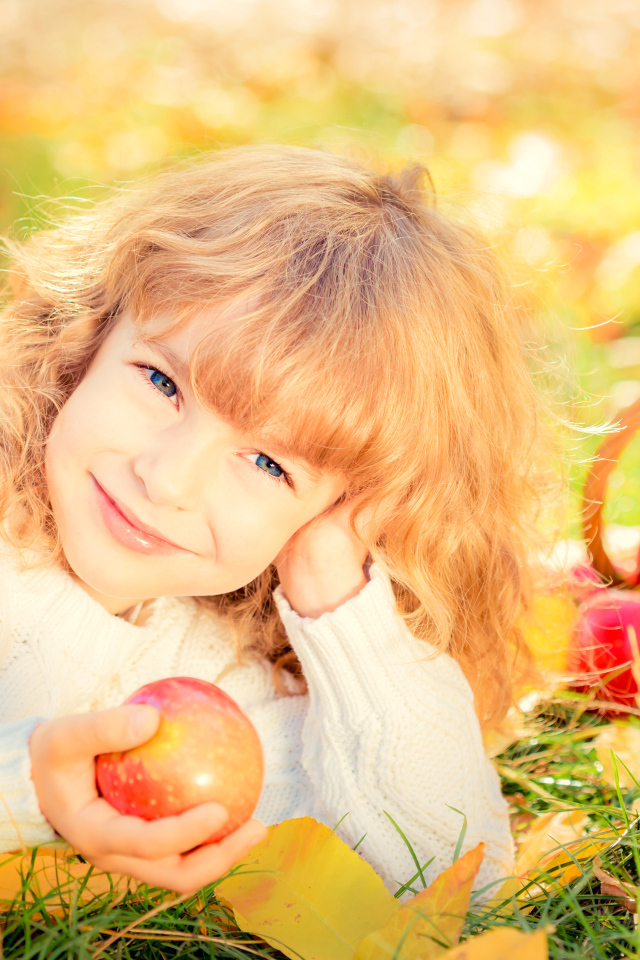 Улыбающаяся рыжеволосая девочка с корзиной красных яблок