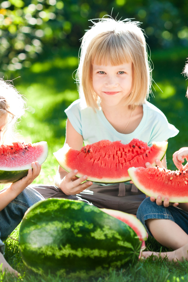 Три маленькие девочки едят арбуз на зеленой траве летом