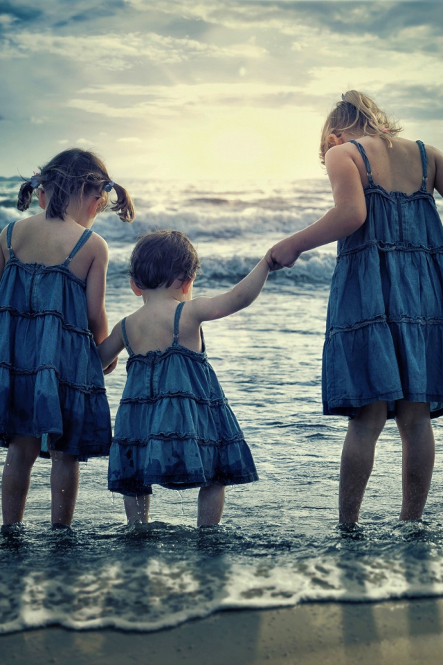 Три маленькие девочки стоят в воде на берегу моря