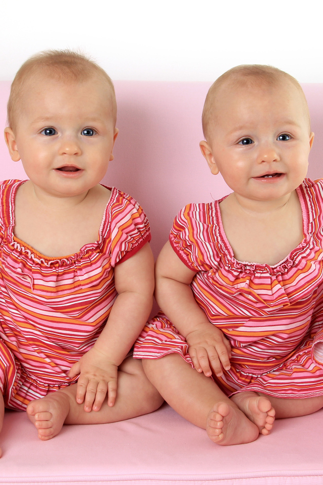 Две милые маленькие девочки сидят на розовом диване