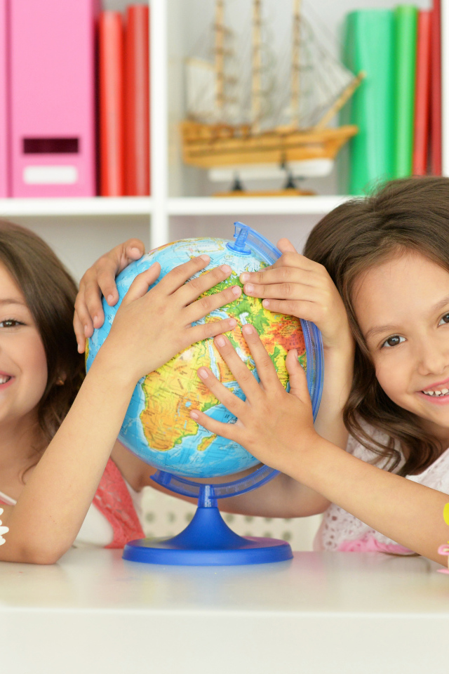 Две маленькие девочки школьницы с глобусом  в руках
