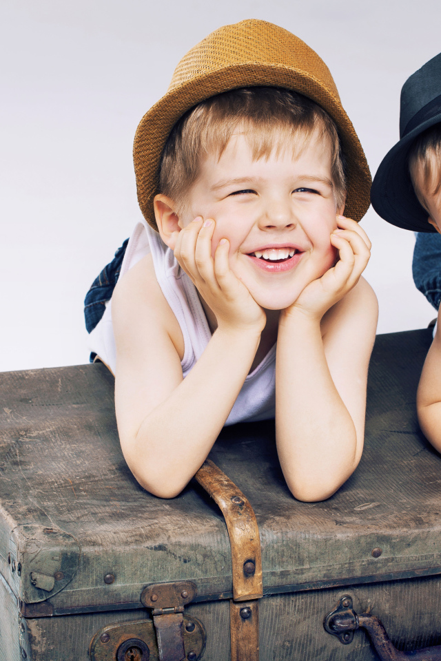 Два маленьких улыбающихся мальчика лежат на старом чемодане