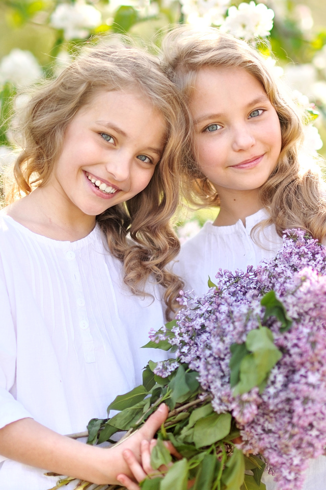 Две улыбающиеся девочки близняшки с букетом сирени