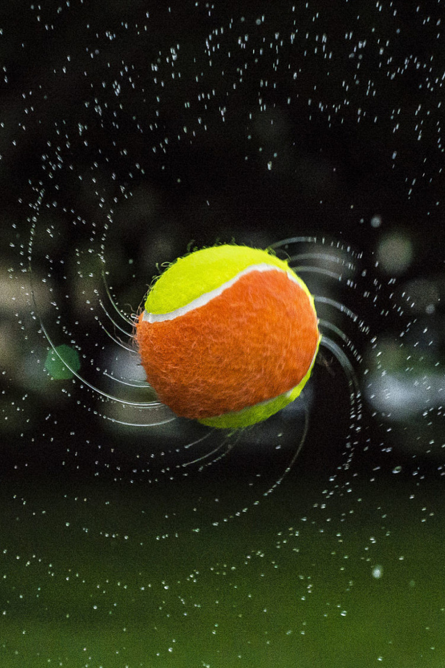 Теннисный мяч летит в каплях воды 