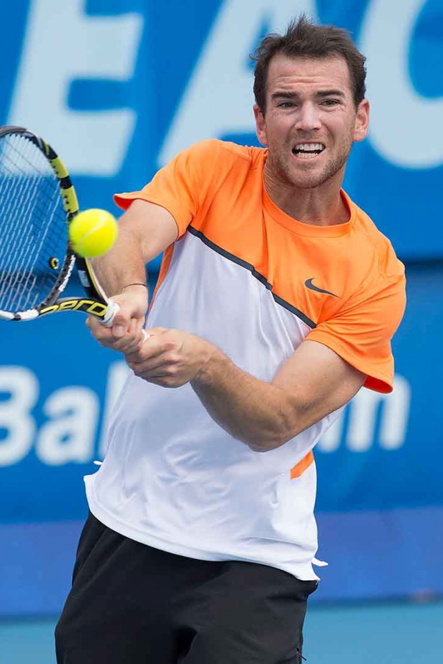 Теннисист Адриан Маннарино отбивает мяч ракеткой 