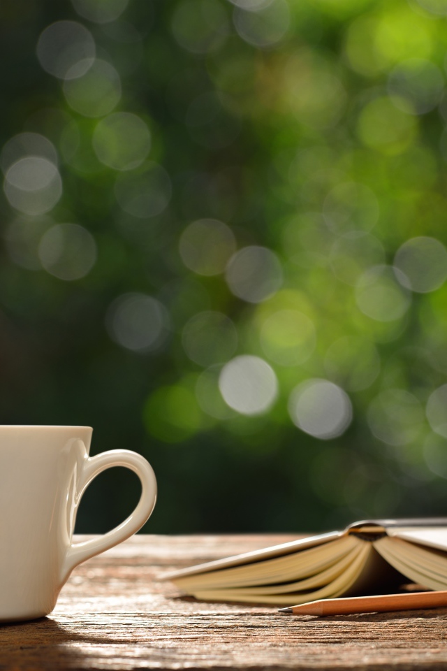 Белая чашка на столе с открытой книгой