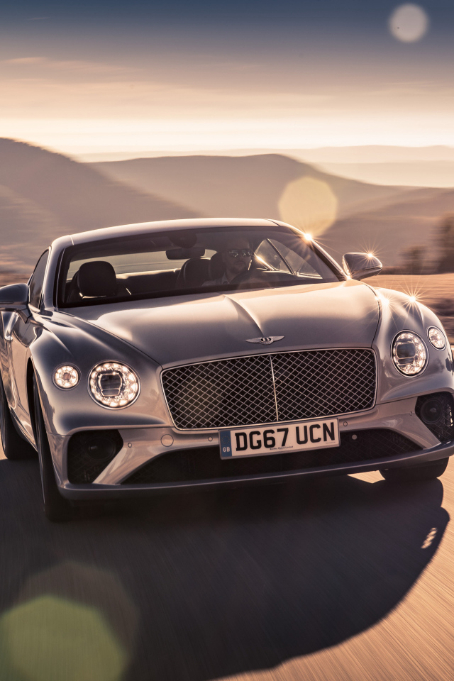 Серебристый автомобиль Bentley Continental GT 2018 года на трассе
