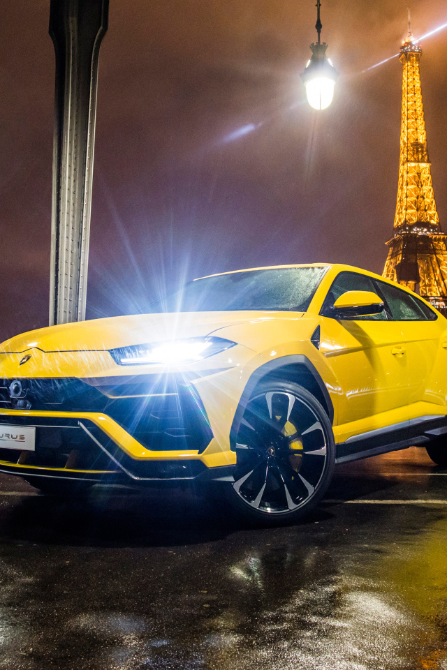 Желтый Lamborghini Urus, 2018 с включенными фарами на фоне Эйфелевой башни