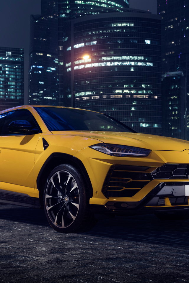 Желтый Lamborghini Urus на фоне ночных небоскребов