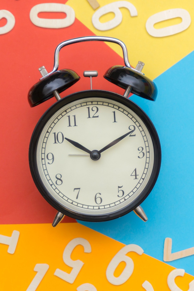 Будильник на разноцветном фоне с цифрами