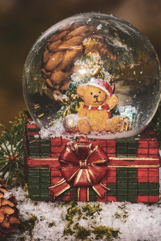 Снежный шар с медвежонком на столе с большой шишкой и еловой веткой 