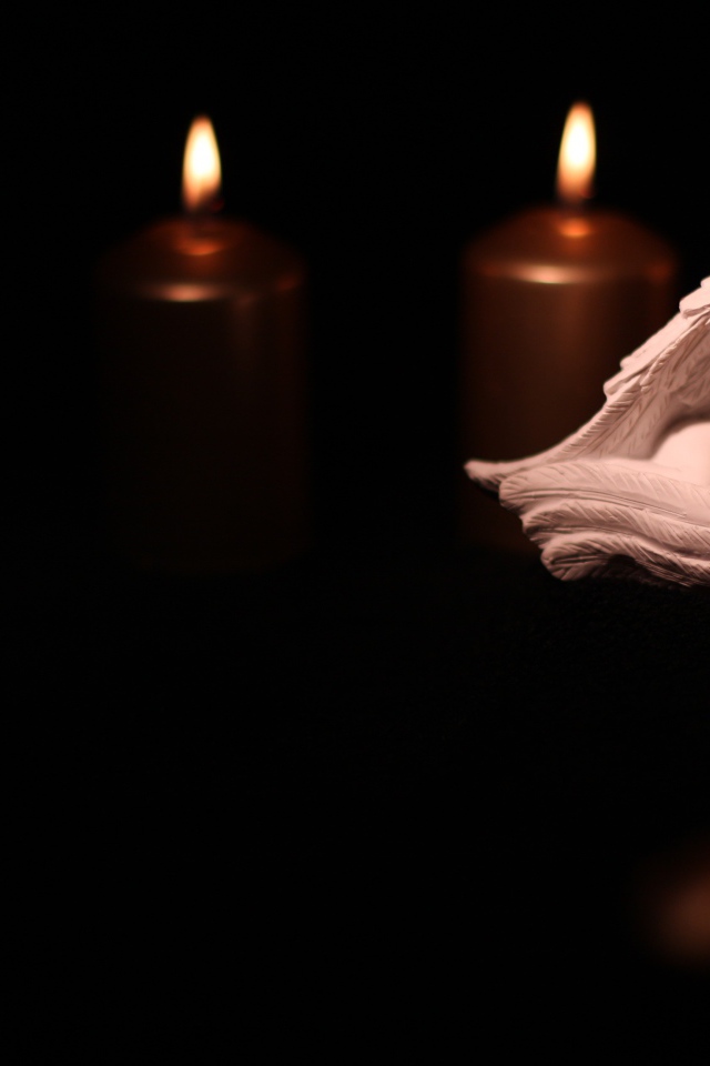 Фигурка ангела освещен горящими свечами на черном фоне