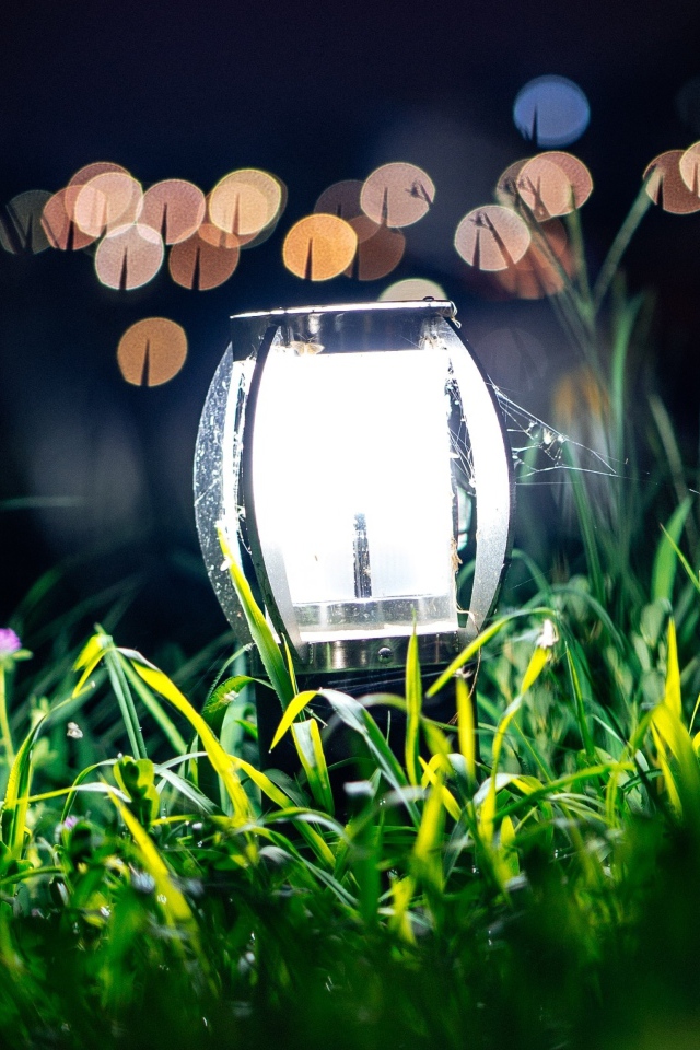 Включенный фонарь стоит в зеленой траве