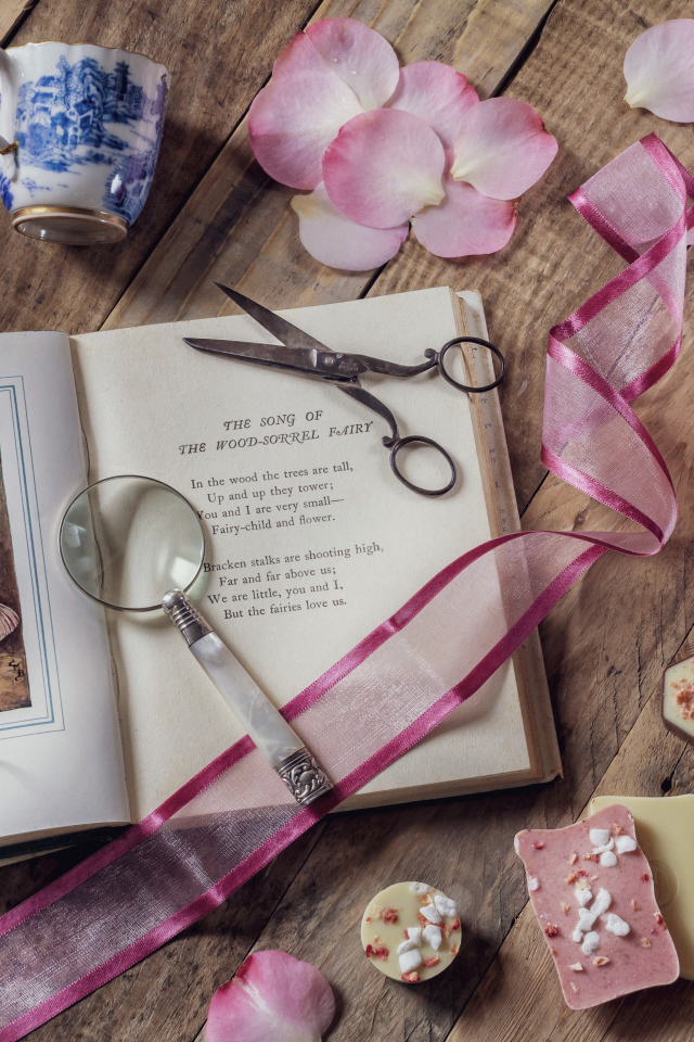 Старая книга на столе с увеличительным стеклом и искусственными цветами