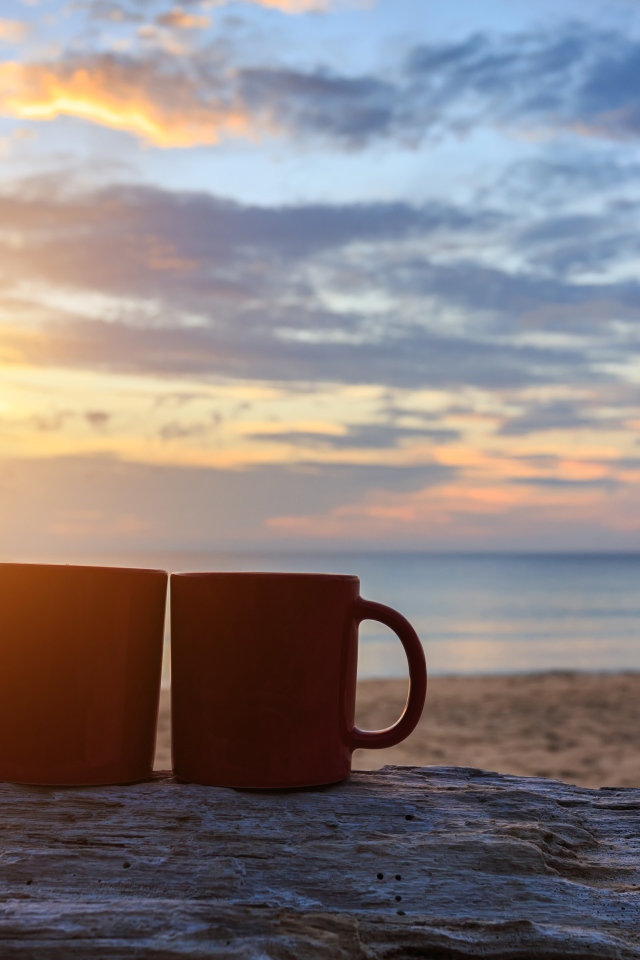 Две чашки стоят на песке на фоне рассвета 