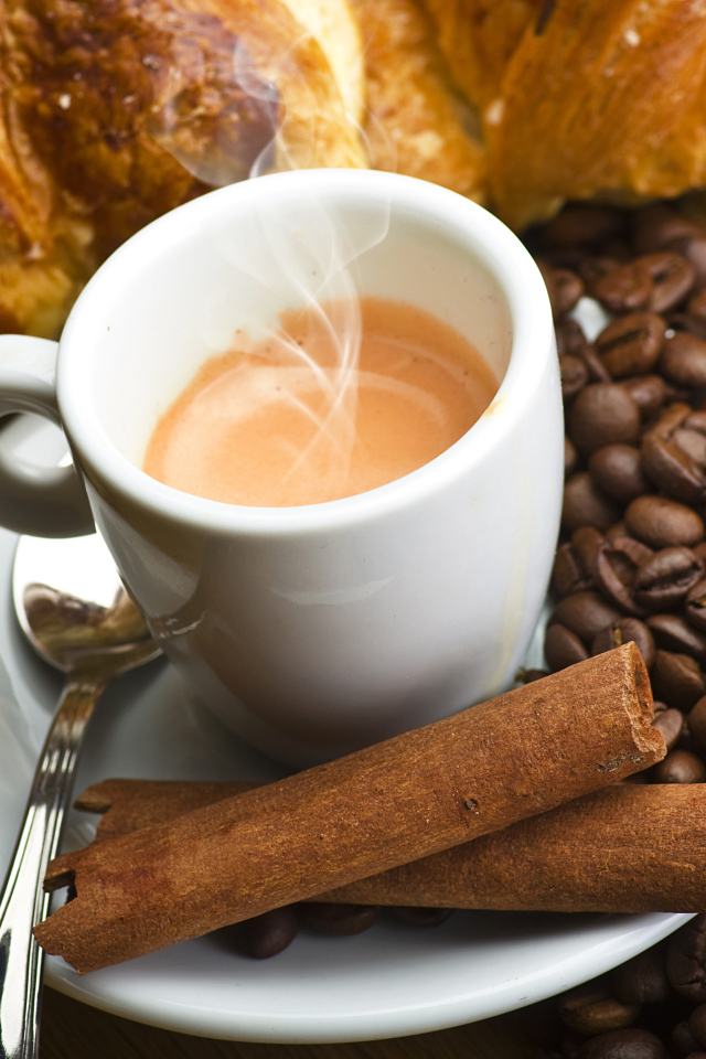 A cup of hot coffee on a table with cinnamon, coffee grains and pastries