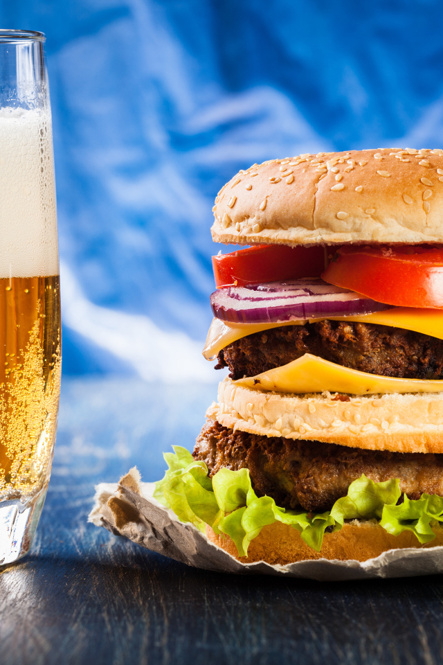 Стакан пива с гамбургером на столе