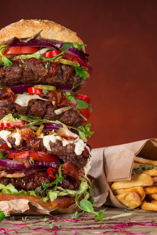 Огромный гамбургер на столе с картофелем фри и острым перцем