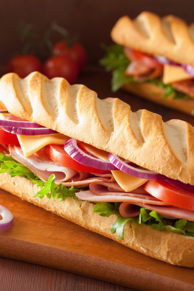 Аппетитный сэндвич с ветчиной, листьями салата, помидорами и луком