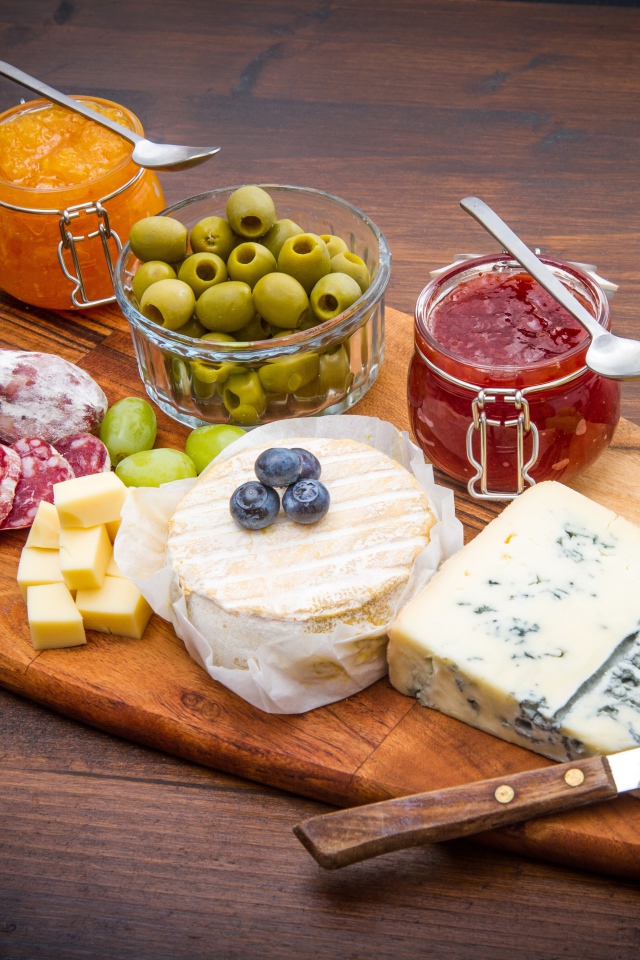Сыр, грибы, маслины, колбаса, виноград и джем на разделочной доске 