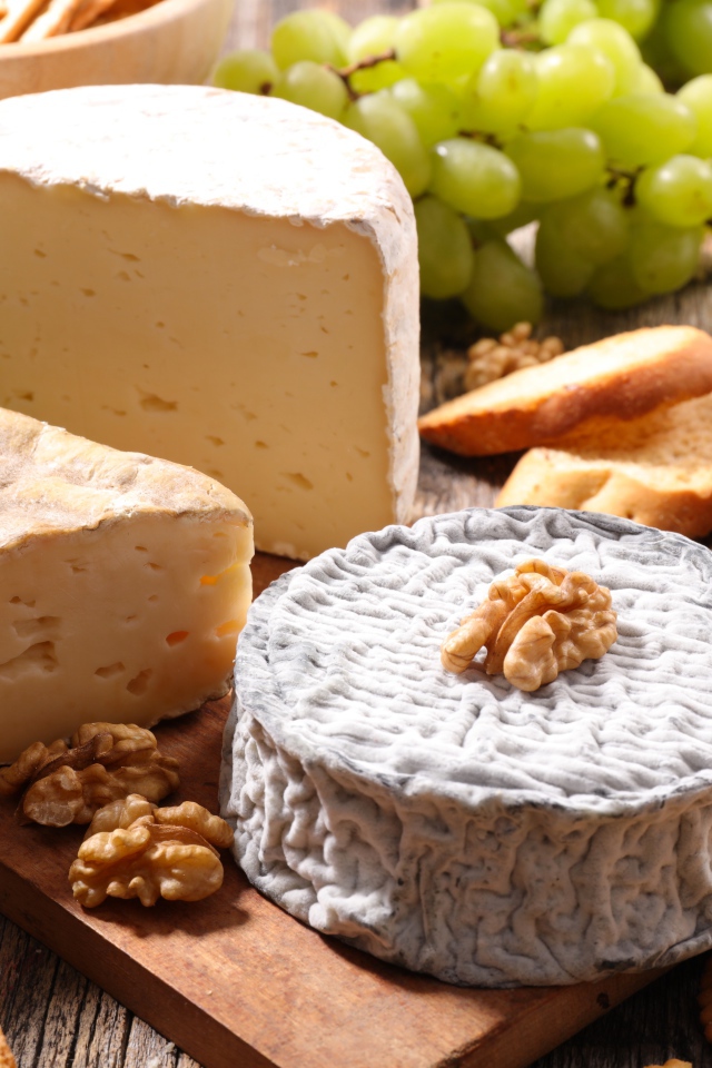 Сыр с плесенью на столе с виноградом, орехами и хлебом