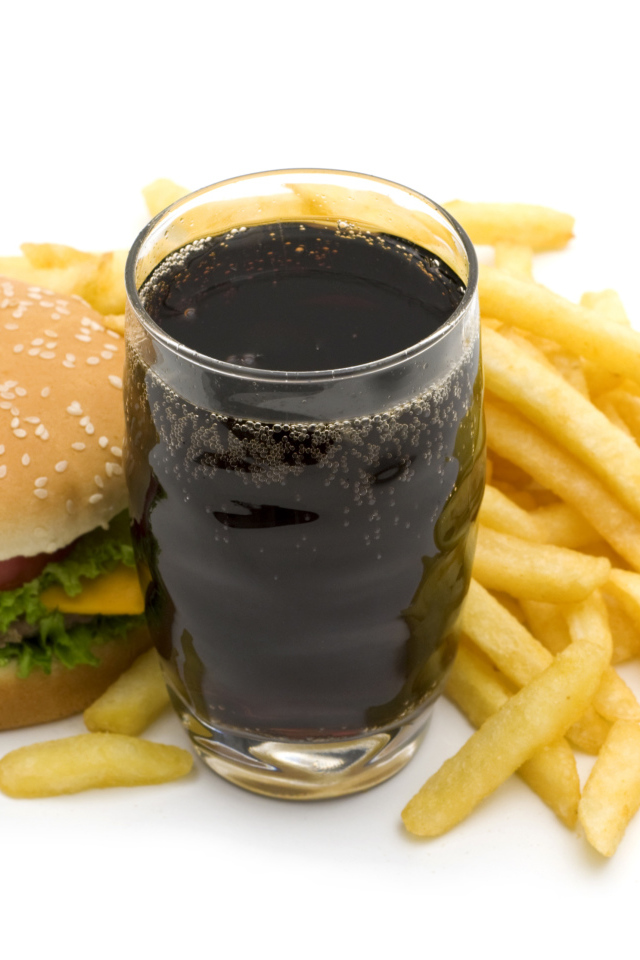 Cola in a glass on a table with a hamburger and french fries on a white background