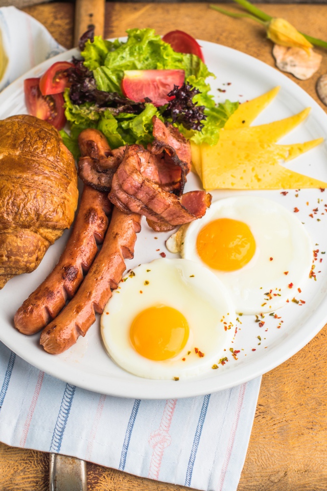 Яичница, салат, сосиски и круассан с соком на завтрак 