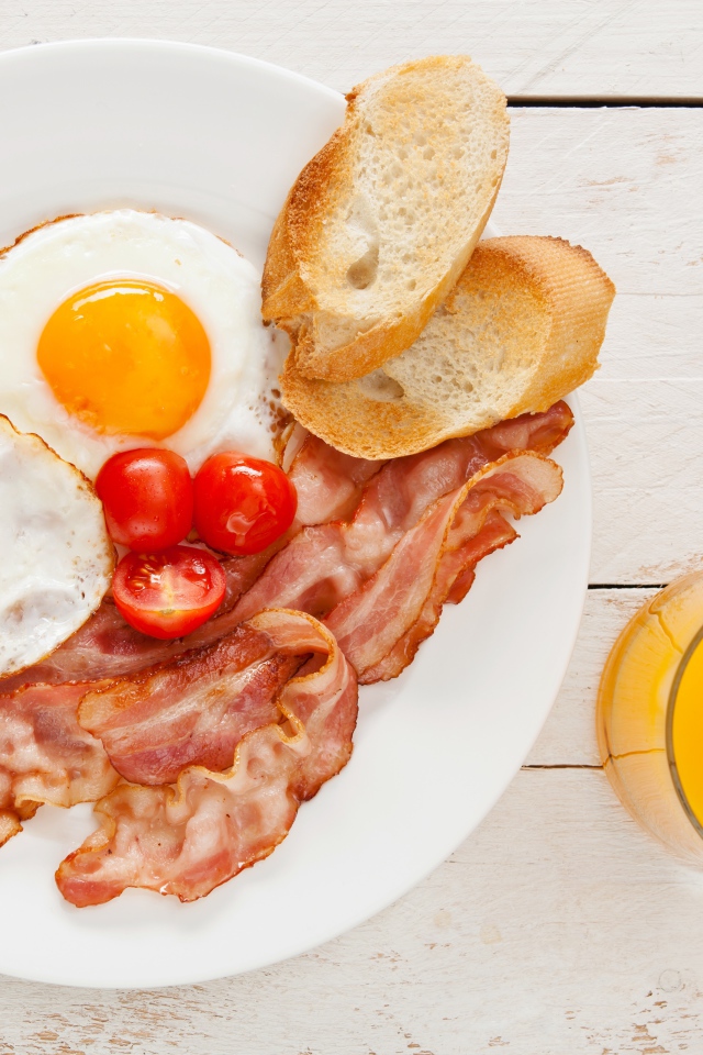 Fried eggs with bacon, croutons and tomatoes on the table with juice